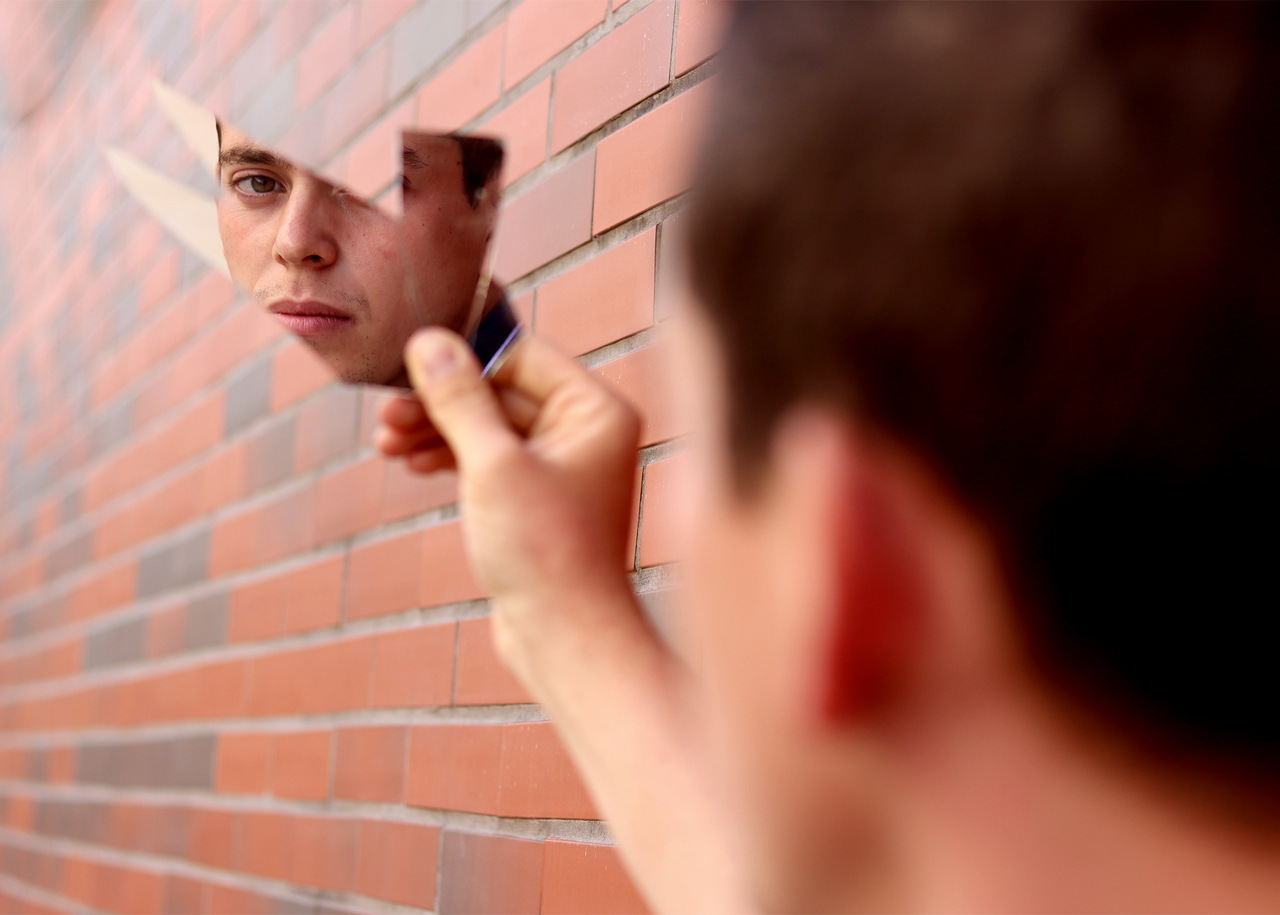 Services A man's face is reflected in a fragment of a mirror held against a brick wall.