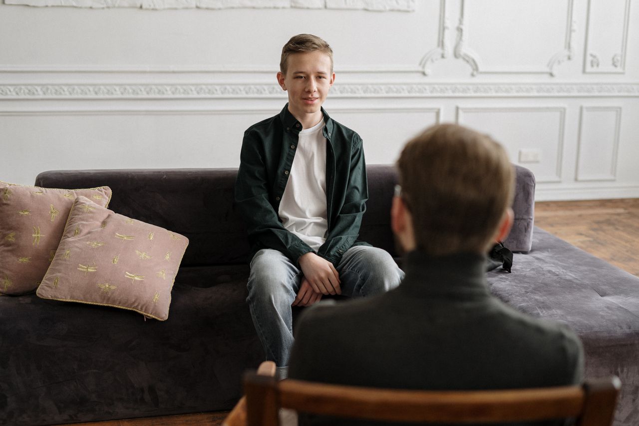 The Art of Drawing Readers In: Your attractive post title goes here A teenage boy in a counseling session with a therapist in a modern loft setting, sitting on a sofa.