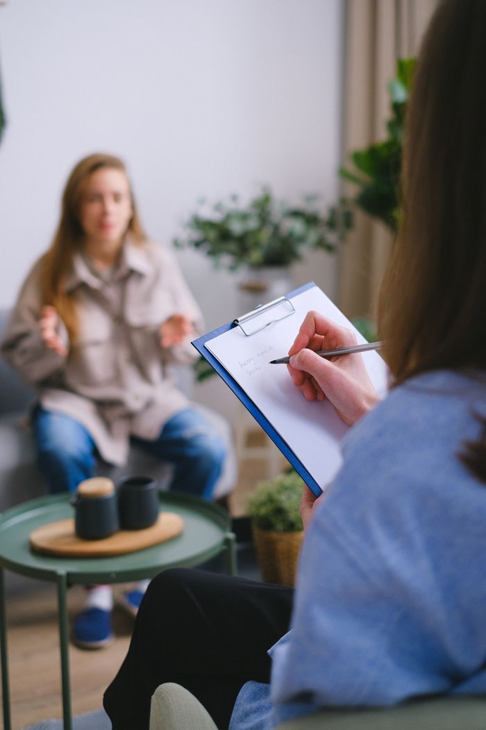 Services Unrecognizable female psychologist taking notes on clipboard while listening to patient sitting on blurred background during psychotherapy consultation in office