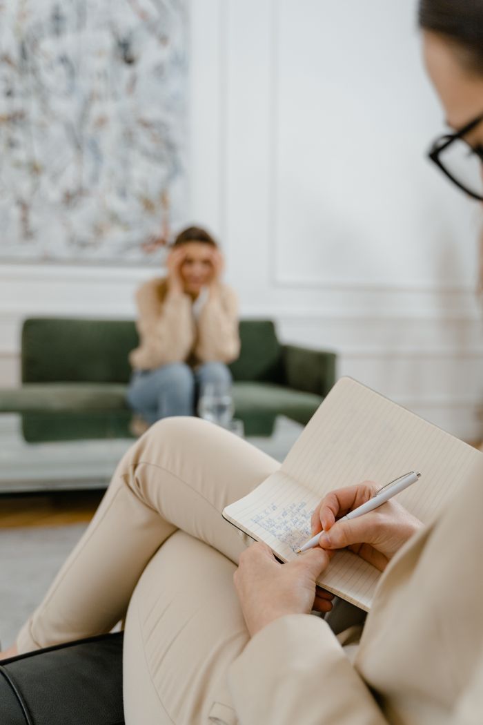 About A therapist takes notes in a modern office setting during a therapy session with a patient.